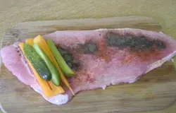 Посыпать свинину специями, на край мяса положить огурец и морковь