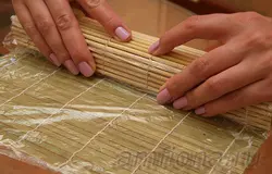 Еще раз накройте ролл ковриком и прижмите рыбу.