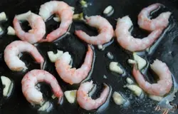 На сковородку кладем кусочек сливочного масла. Когда масло растает, высыпаем почищенные креветки и порезанный зубок чеснока. Обжариваем креветки 30-60 секунд.