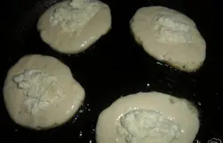 На разогретую с растительным маслом сковороду выложить столовую ложку теста, наверх положить начинку из творога, и снова накрыть тестом.