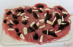 Порезанные чеснок и чернослив выкладываем на мясо.