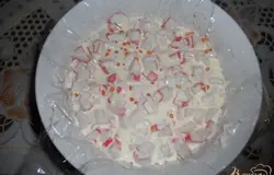 Далее выкладываем нарезанное крабовое мясо. Снова поливаем "кремом". Не бойтесь переборщить с заливкой, крем прекрасно застынет.