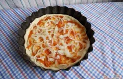Тесто выкладываем в смазанную подсолнечным маслом форму для духовки так, чтобы получились небольшие бортики. Смазываем тесто томатным кетчупом. Лук чистим и нарезаем тонкими полукольцами, выкладываем первым слоем на тесто.