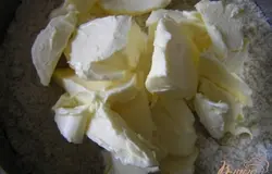 Добавить размягченное сливочное масло и сахар, хорошо перемешать, замешивая тесто.