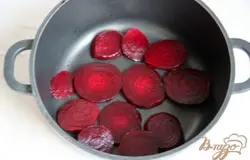 На дно кастрюли для тушения/чугунка выкладываем ломтики нарезанной сырой свеклы.