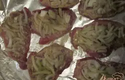 Выложить мясо на противень, сверху на каждый кусок мяса положить тонко нарезанный лук.